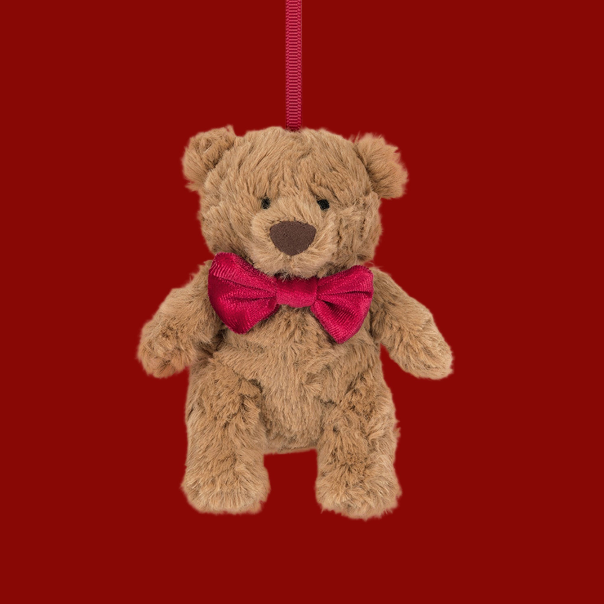 A bear shaped stuffed animal ornament wearing a red bow. 