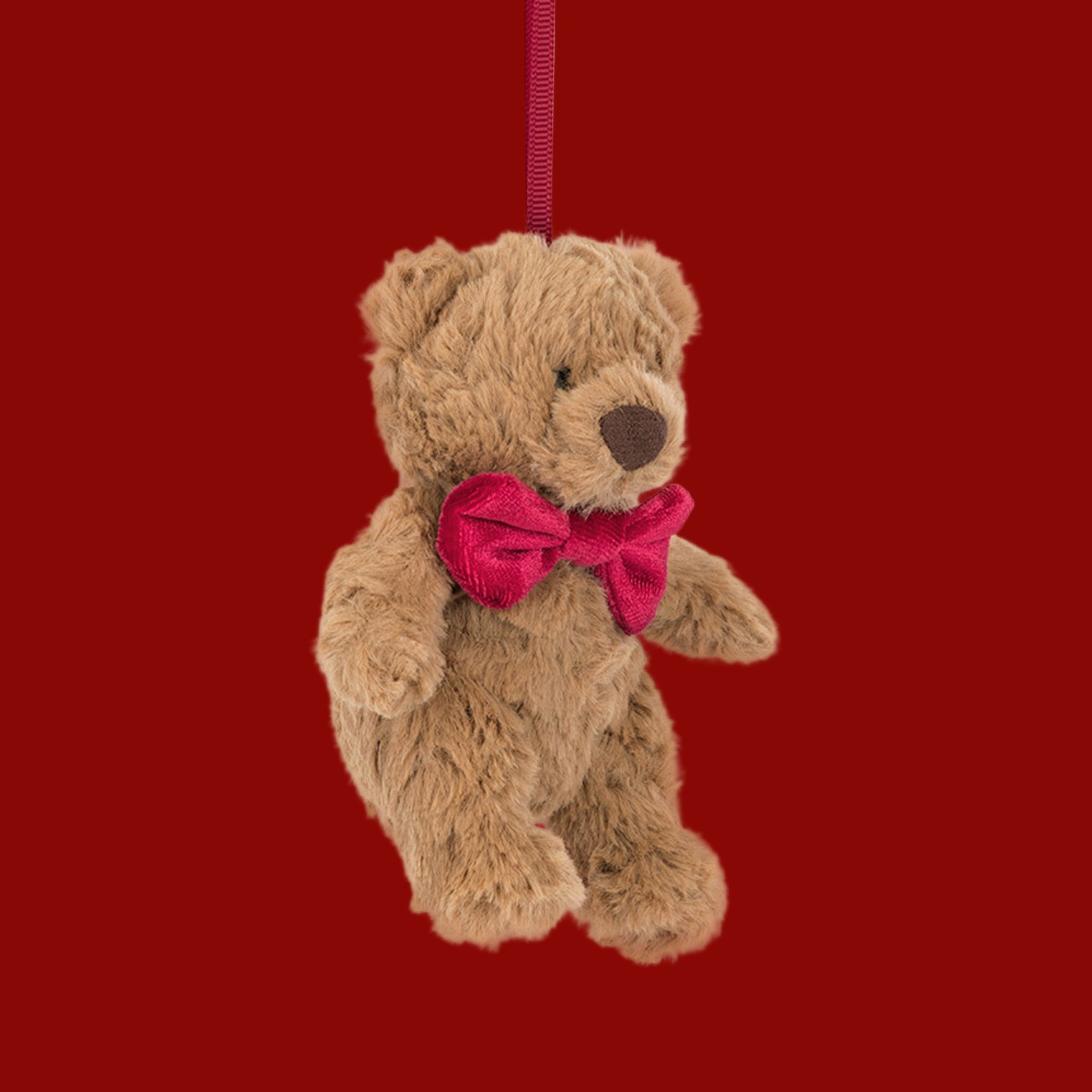 A bear shaped stuffed animal ornament wearing a red bow. 