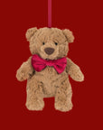 A bear shaped stuffed animal ornament wearing a red bow. 