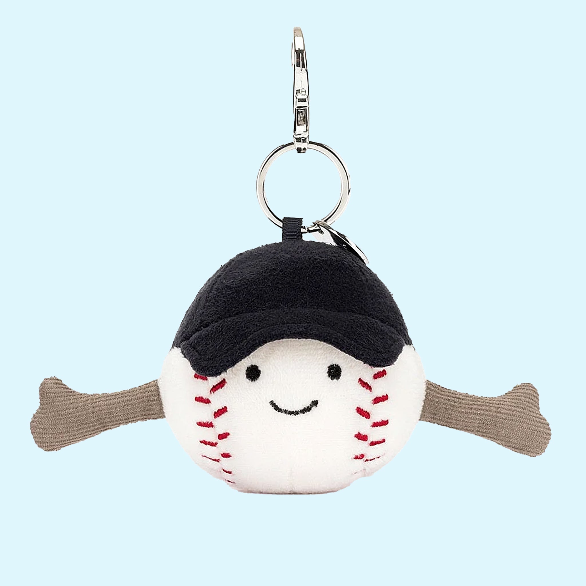 On a blue background is a baseball shaped stuffed toy attached to a keychain to make an adorable bag charm. 
