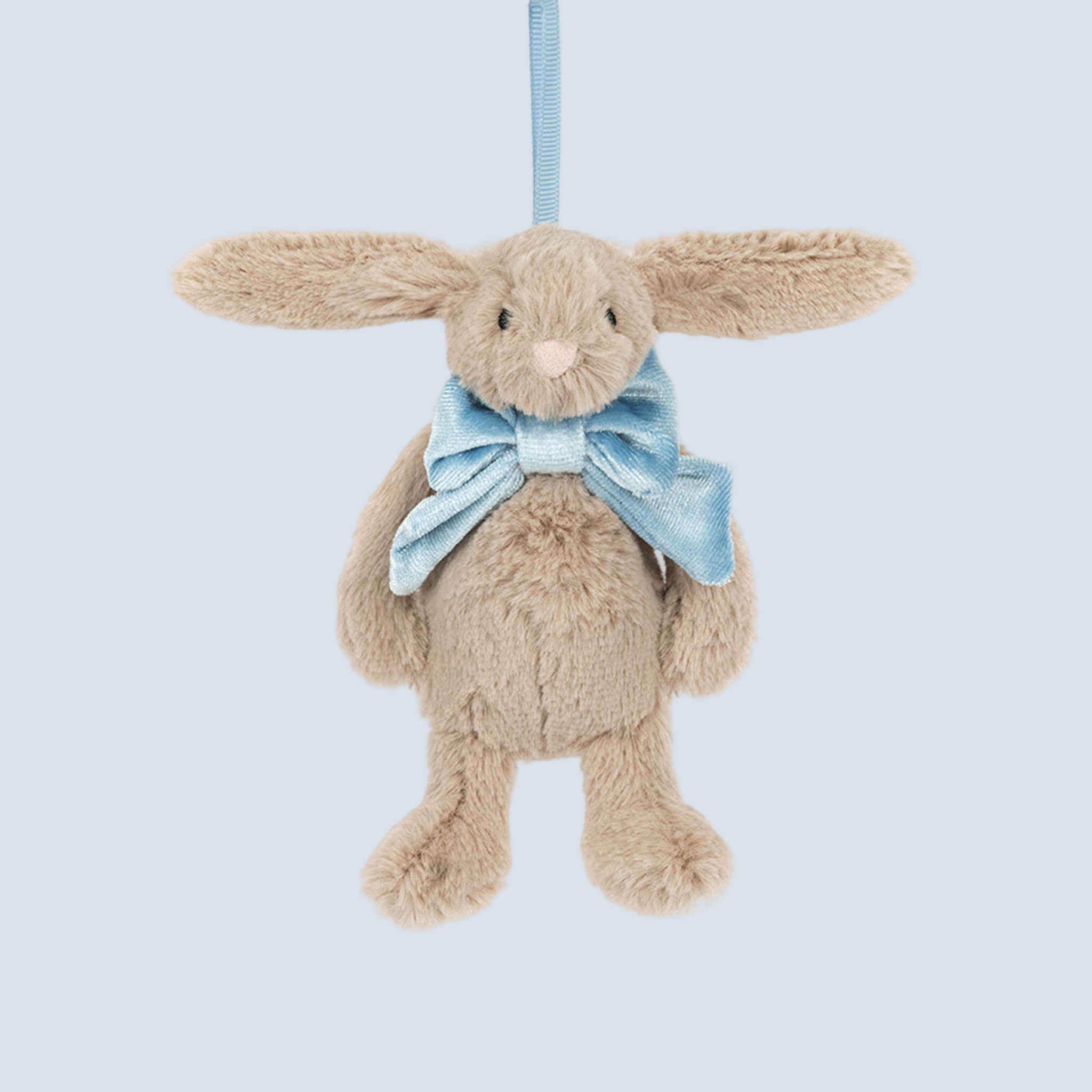 A beige bunny shaped ornament wearing a blue bow. 