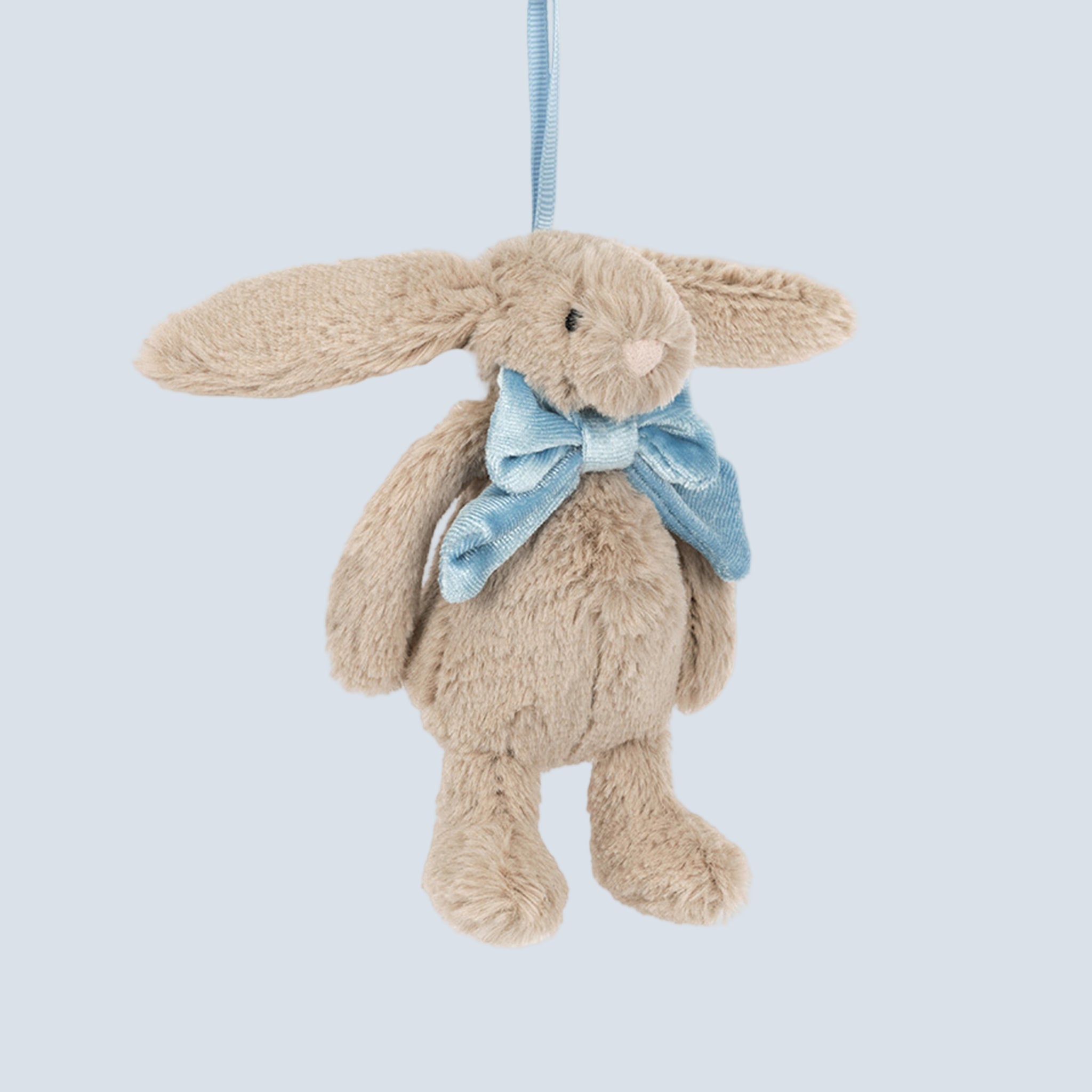 A beige bunny shaped ornament wearing a blue bow. 