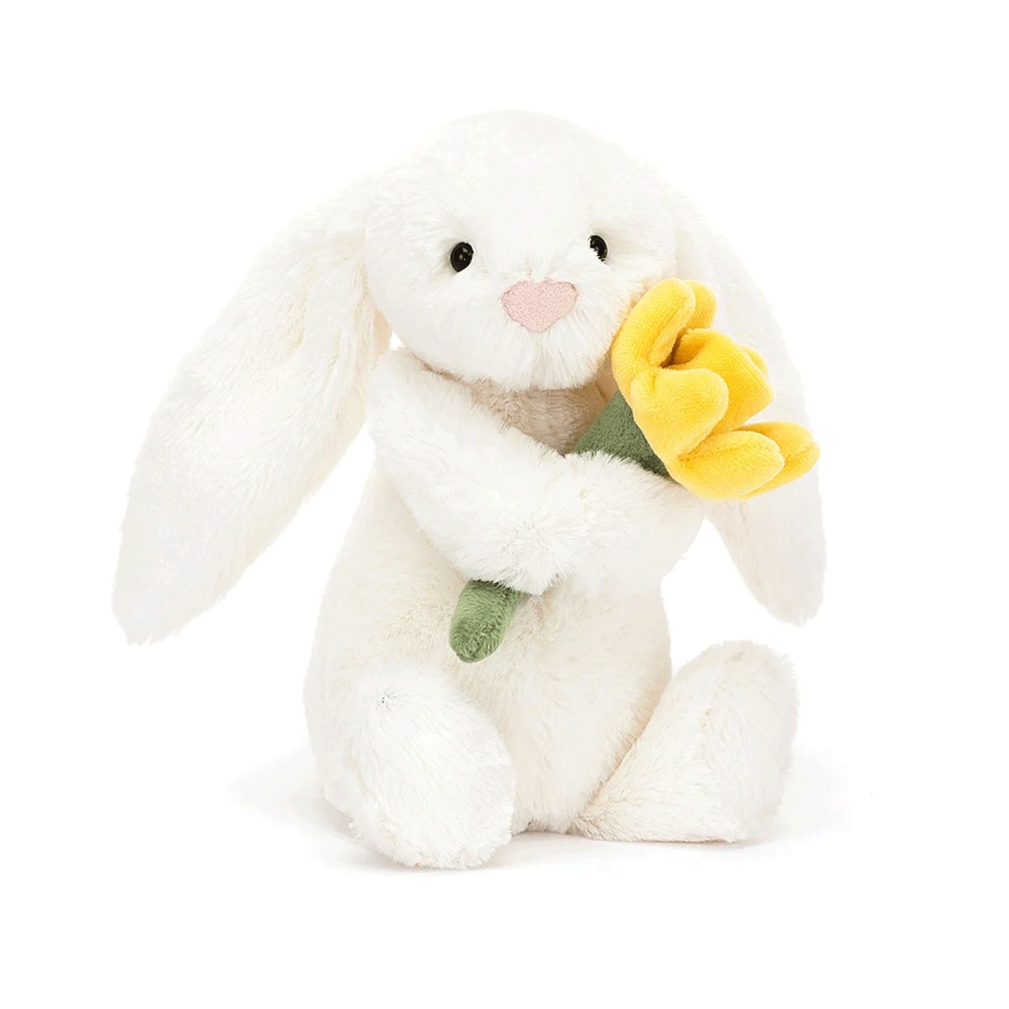 On a white background is a fuzzy white bunny stuffed animal toy with long floppy ears and holding a stuffed daffodil. 