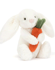 On a white background is a white stuffed toy bunny with long floppy ears and holding an orange stuffed toy carrot. 
