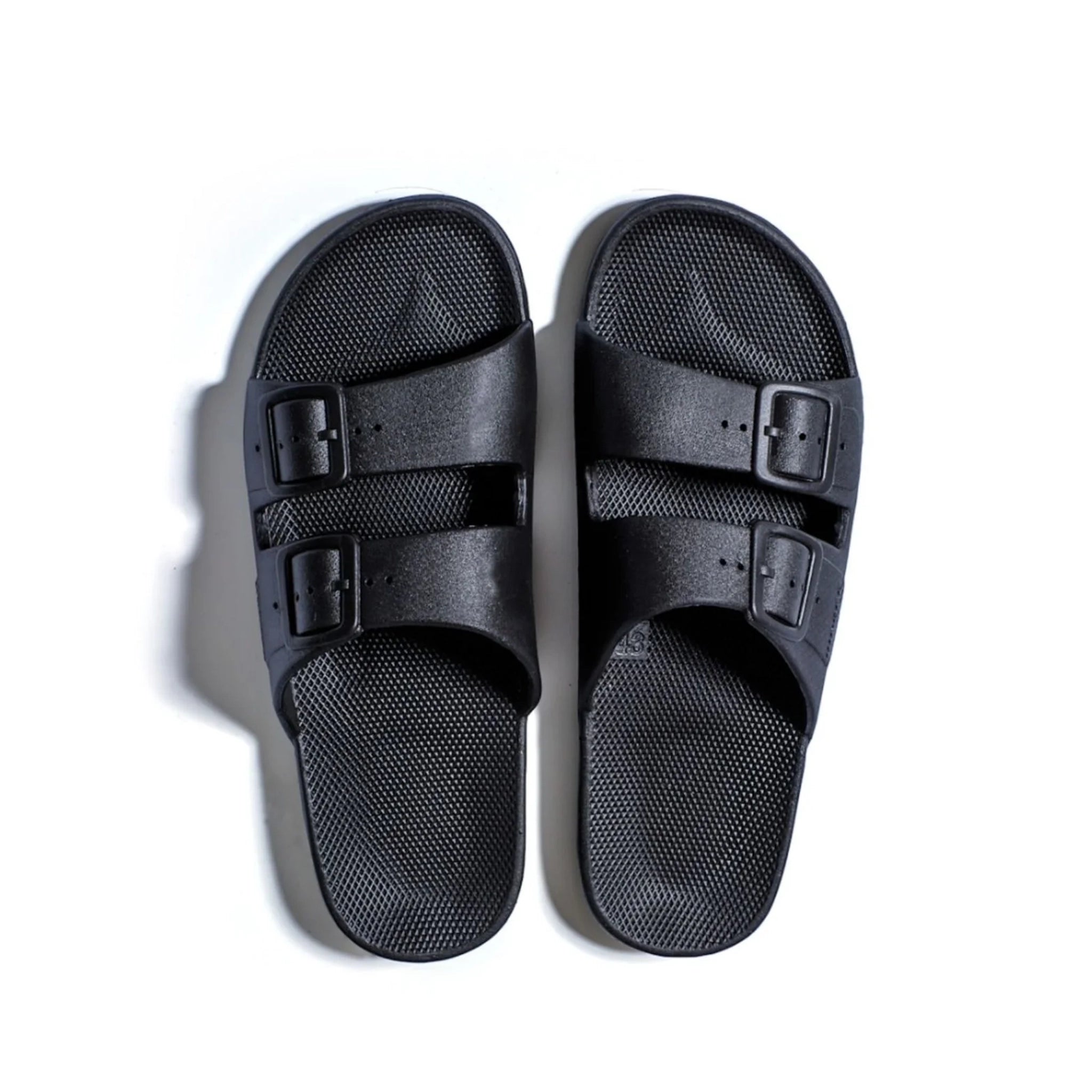 On a white background is a pair of black cloud slides with two straps across the front. 