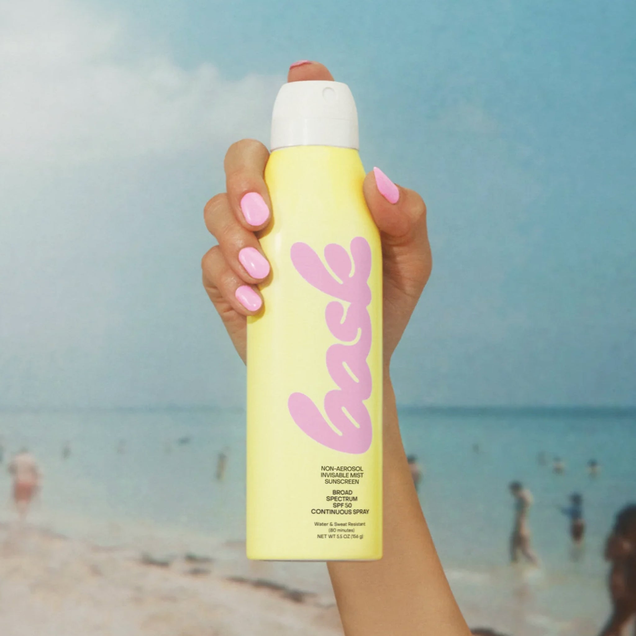 A yellow bottle of spray sunscreen with pink text that reads, "bask".  