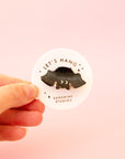 A black speckled bat shaped mini hair clip on a round piece of packaging that reads, 'Let's Hang Sunshine Studios'. 