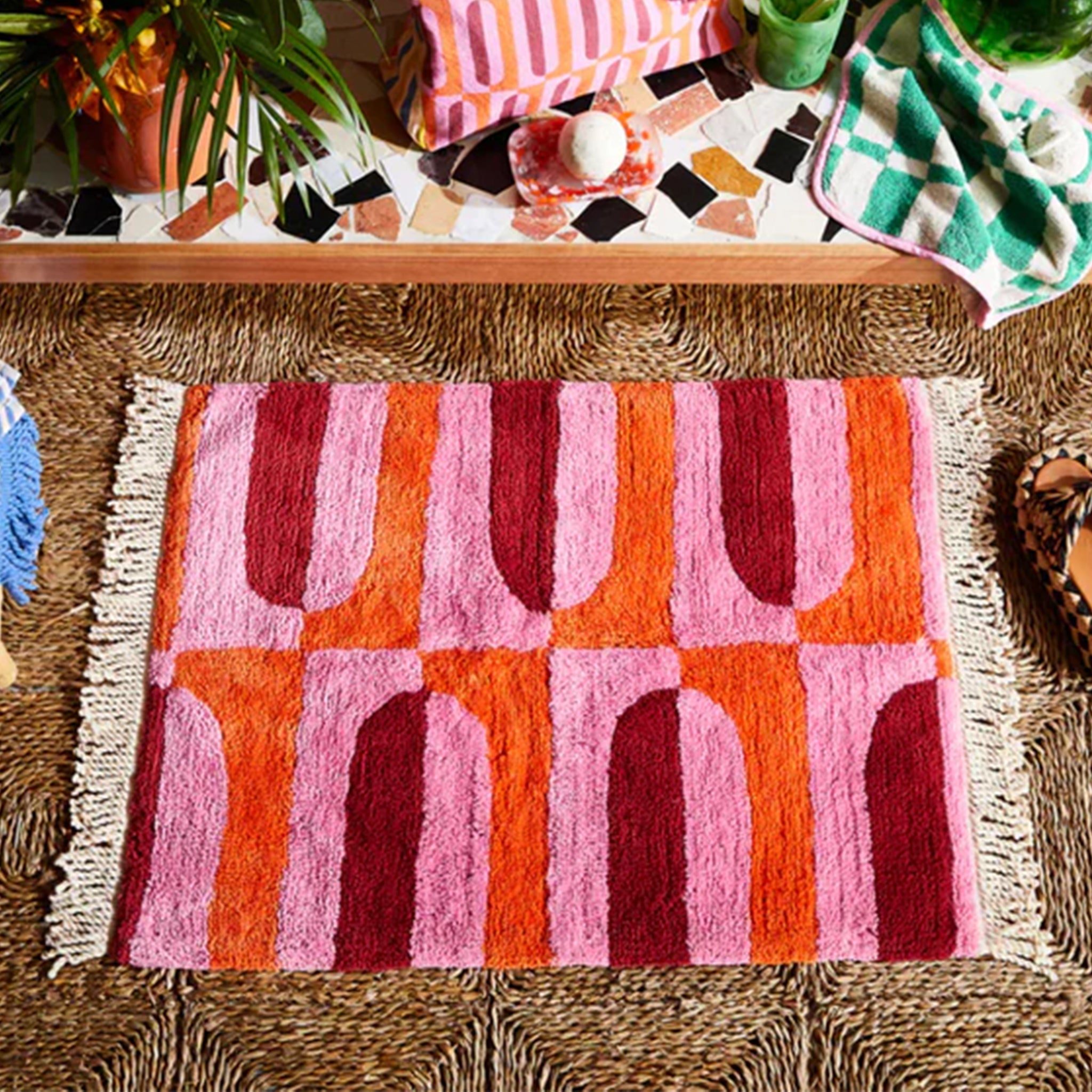 A pink, orange and red bath mat with a tassel detail on each end.