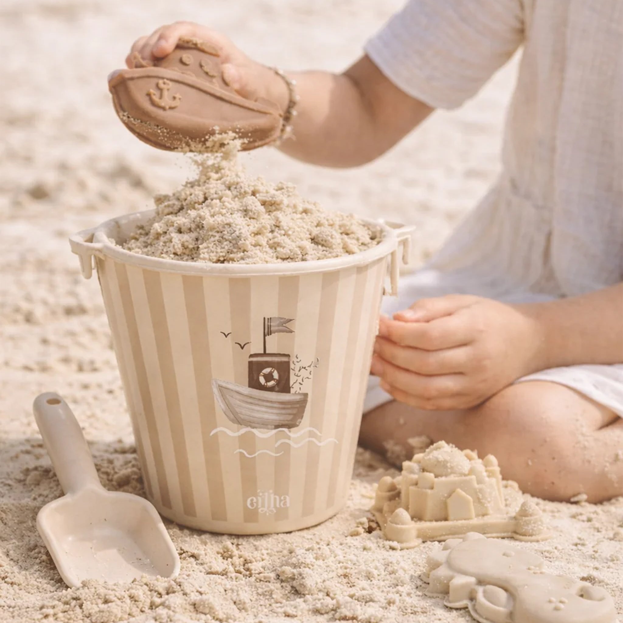 Child playing with sand in a decorative bucket on a sandy surface