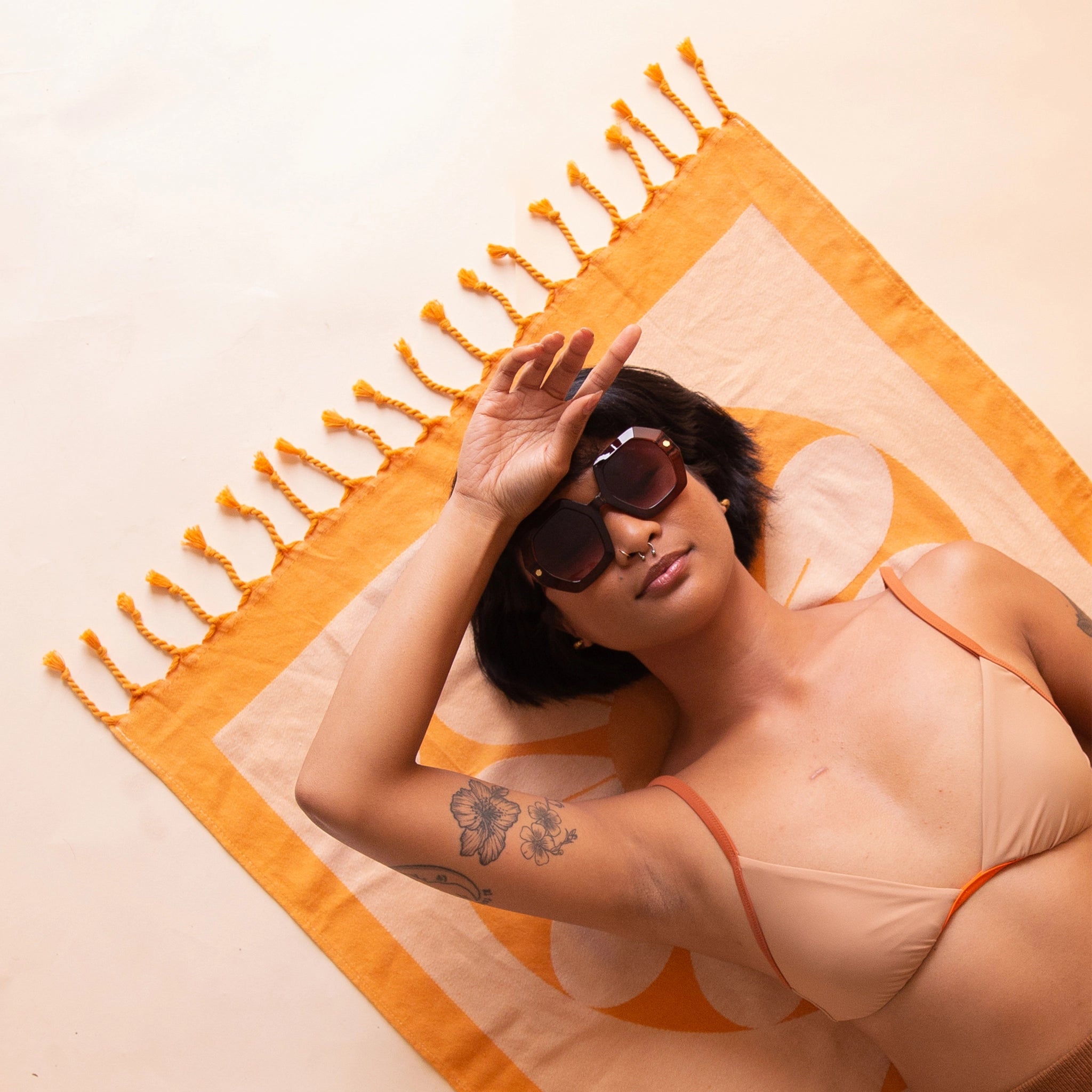 A model laying on the Retro Flower Beach Towel that has two tones of orange and peach along with orange string tassels on the end. 