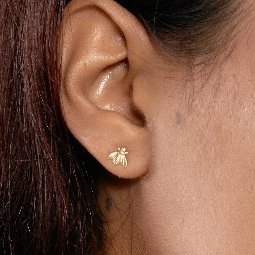 Small gold bee charm stud earrings modeled on an ear