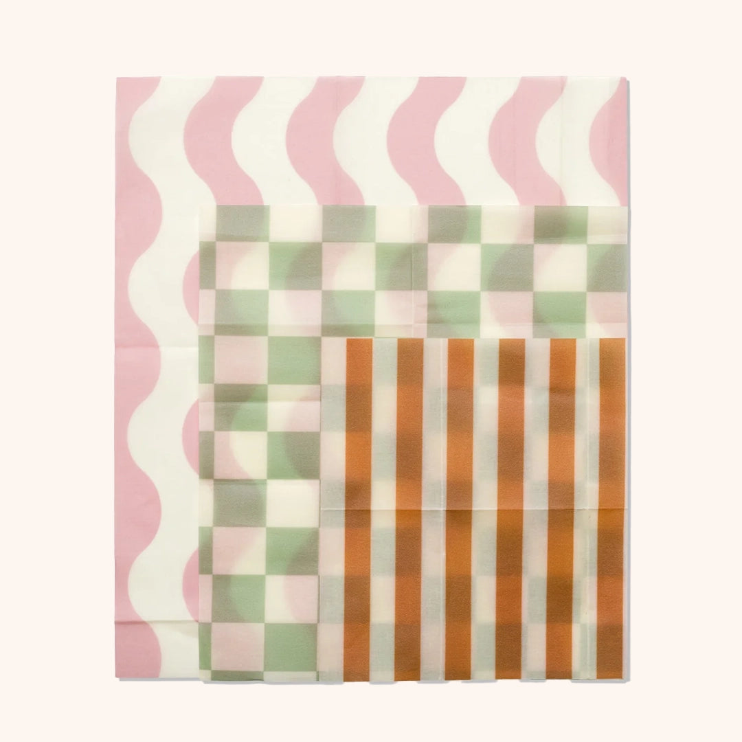 All three beeswax wraps photographed together. It features a pink wavy stripe, a green checkered print and an orange and white stripe. 