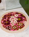 A pink, green and white floral print circular bath mat with a fringe detail around the edge. 