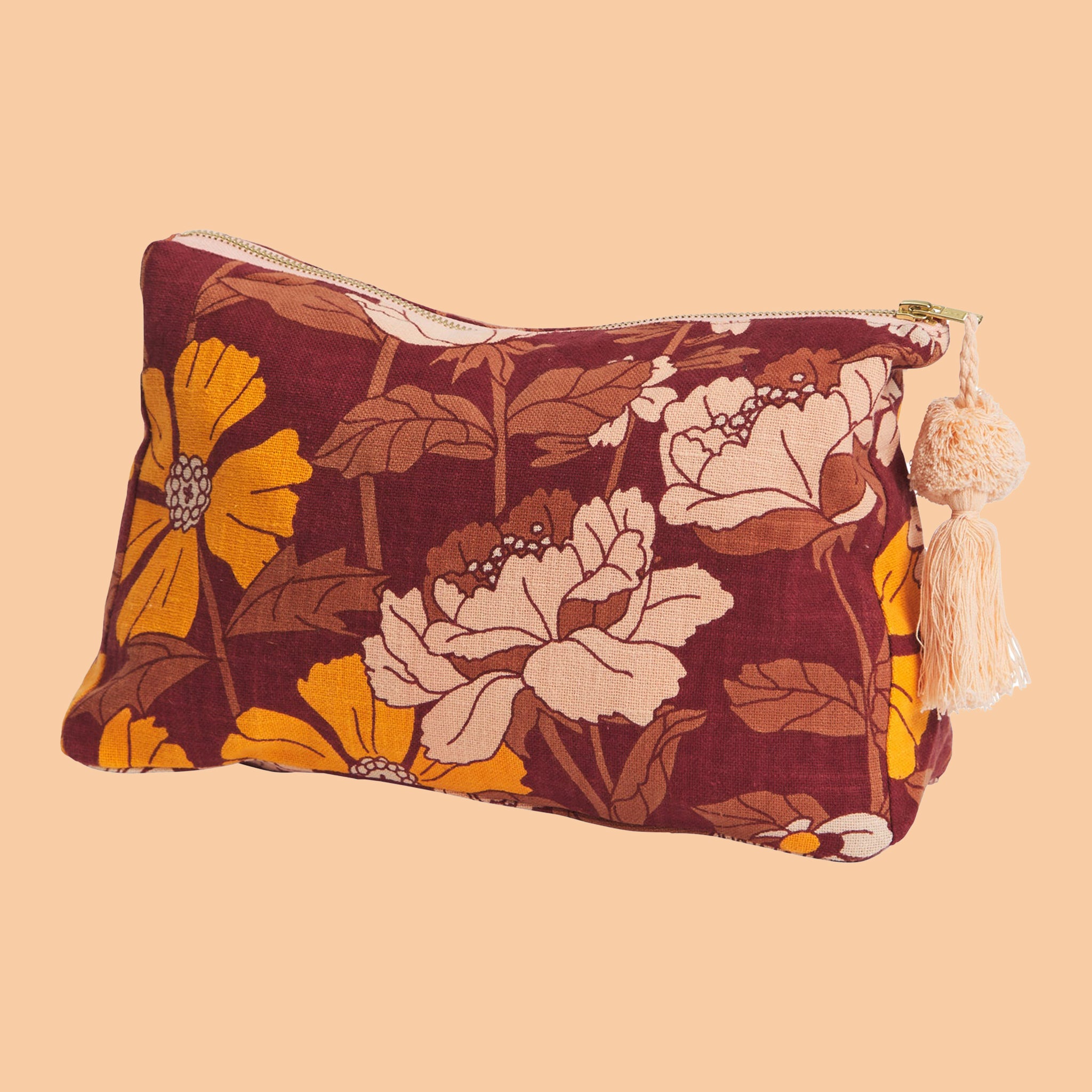 A rust, mustard yellow and cream floral print cosmetic bag with a zip closure and a tassel attached to the zipper. 