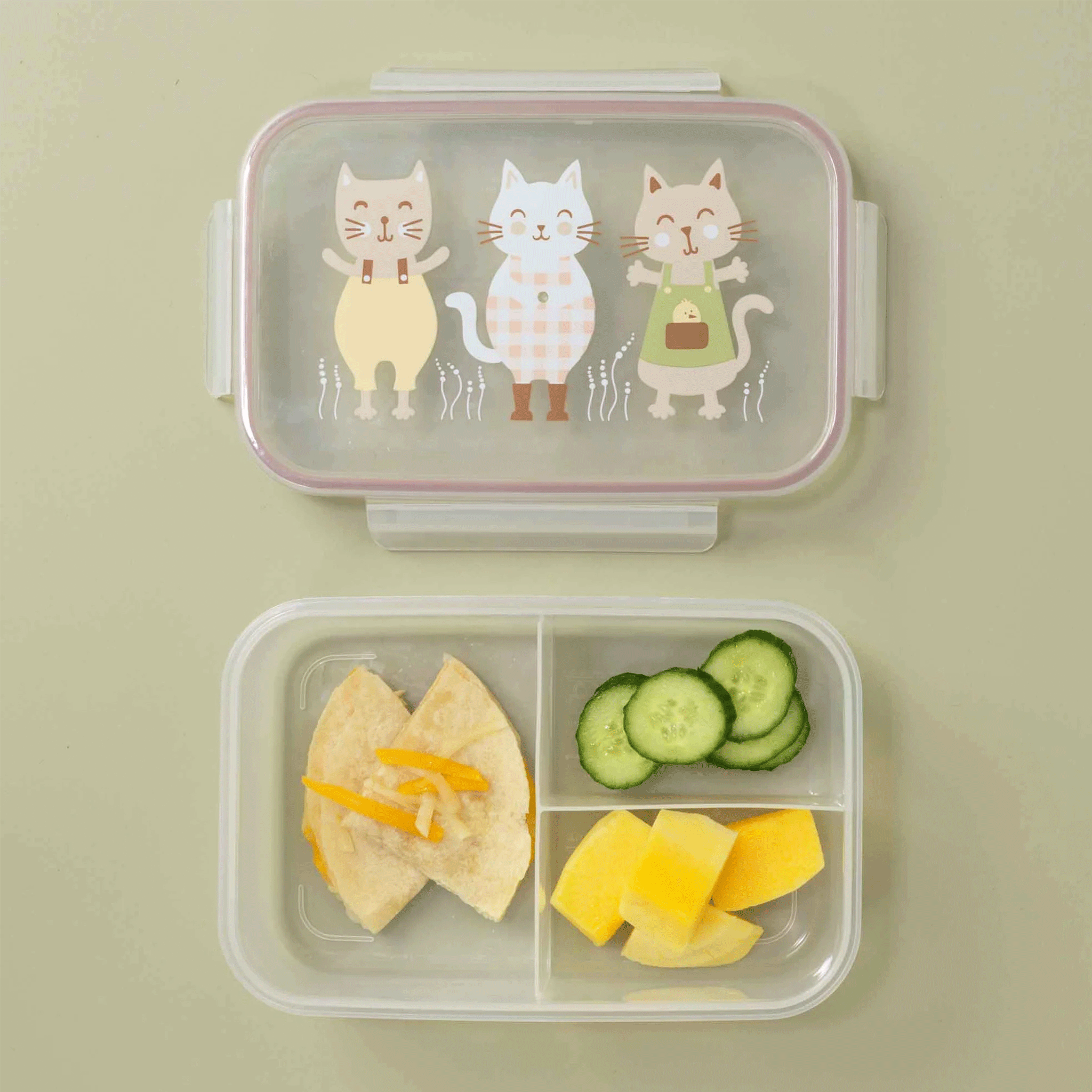 On a green background is a clear plastic bento box with three kitty graphics on the lid filled here with a lunch. 