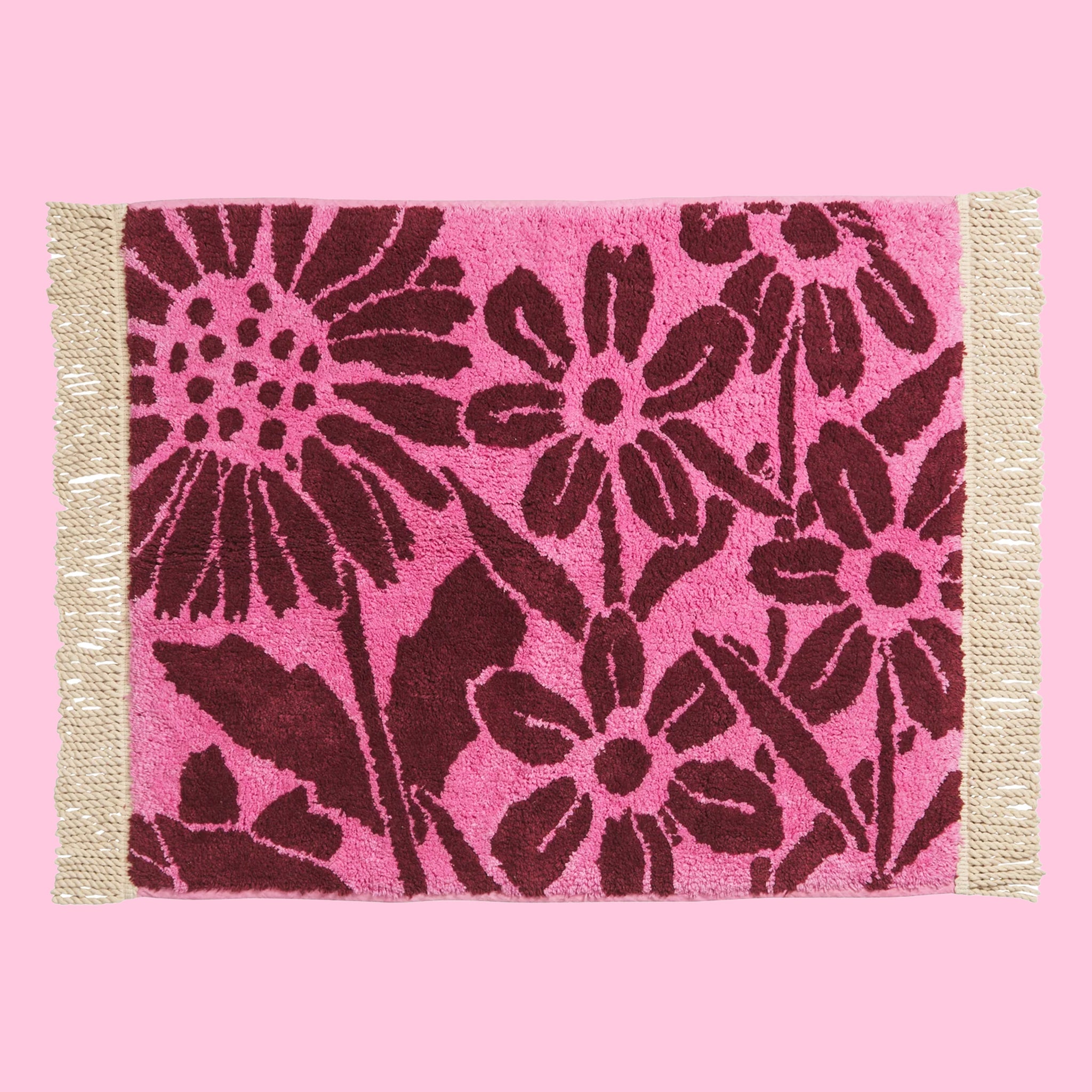 A pink and dark burgundy floral print bath mat with twist fringe details on two ends.