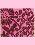 A pink and dark burgundy floral print bath mat with twist fringe details on two ends.