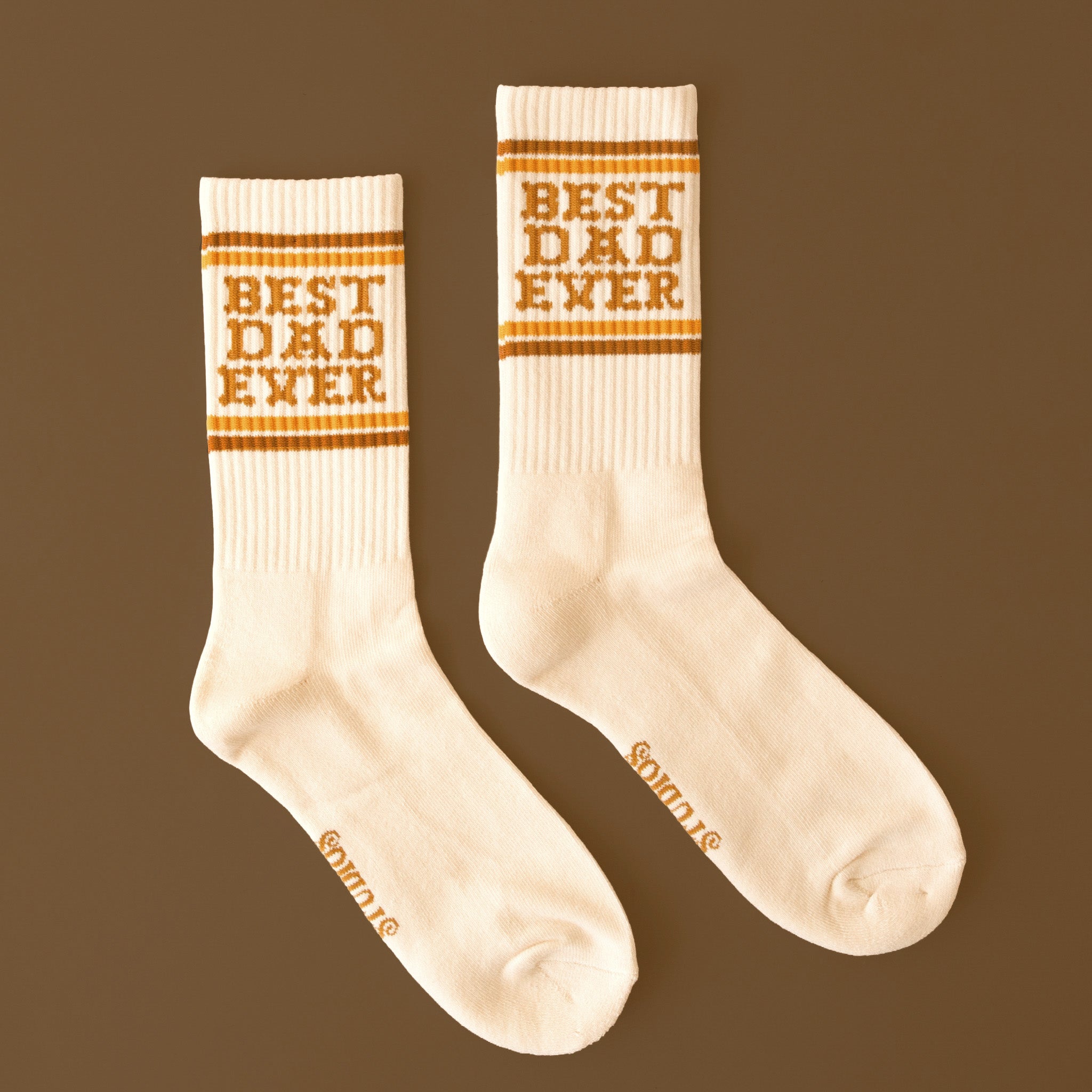 White crew tube socks with brown writing that reads "Best Dad Ever" and gold stripes on a brown background. 