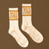 White crew tube socks with brown writing that reads "Best Dad Ever" and gold stripes on a brown background. 