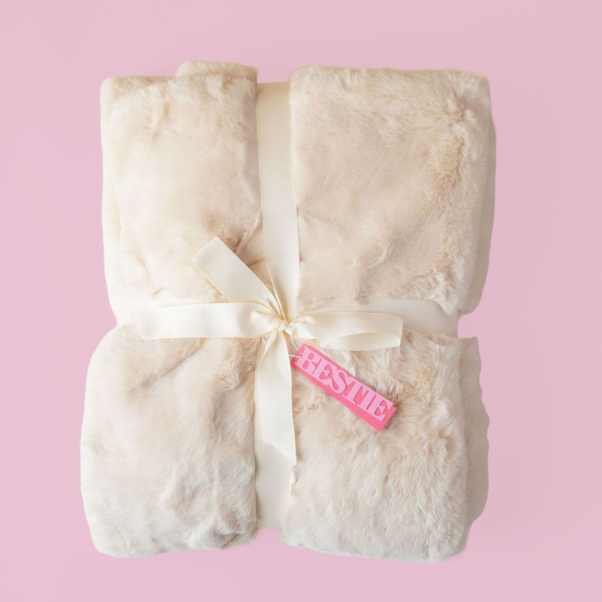 A white fur blanket with a satin ribbon and a pink tag that reads "bestie" tied onto it.