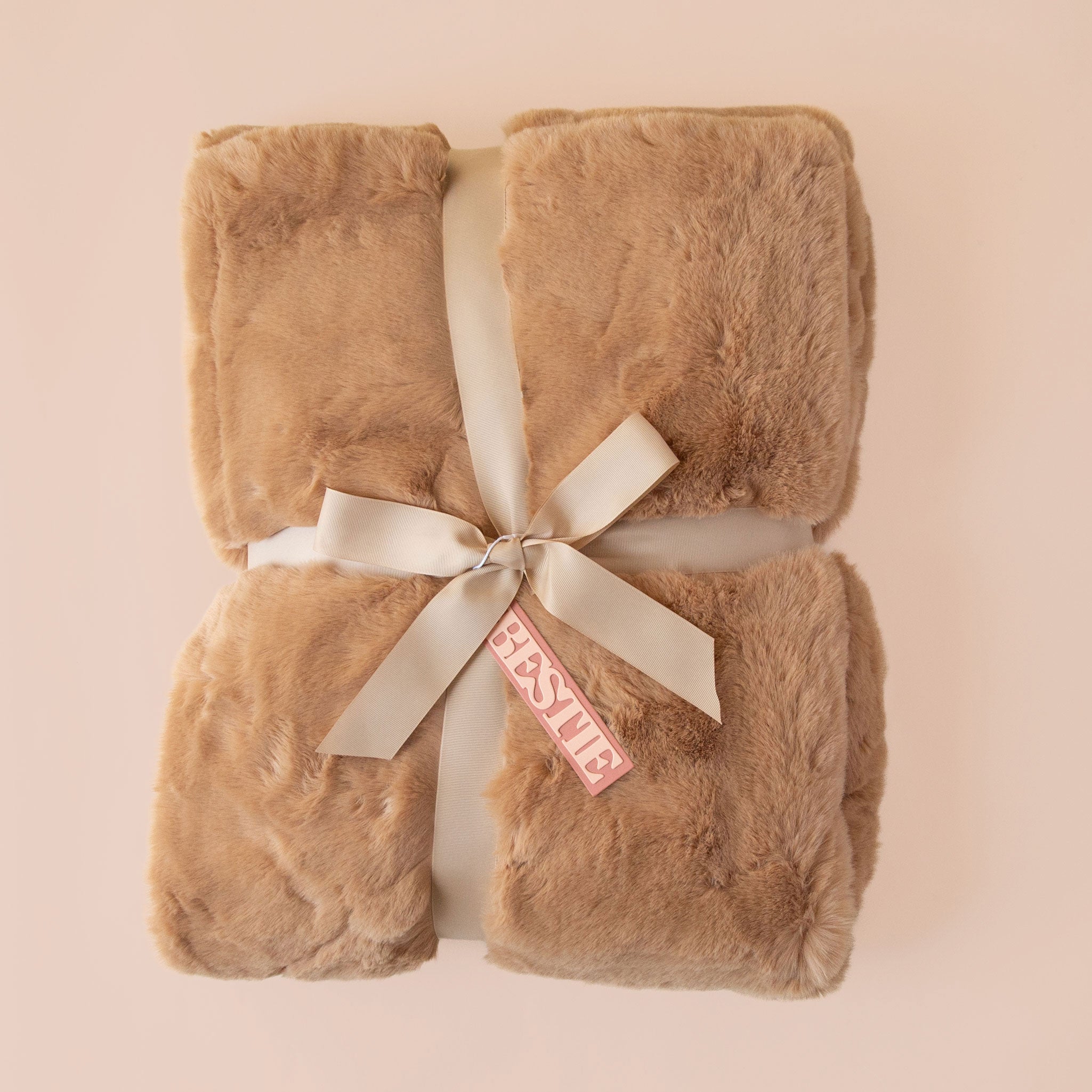 A brown fur blanket with a satin ribbon and a tan tag that reads "bestie" tied onto it.