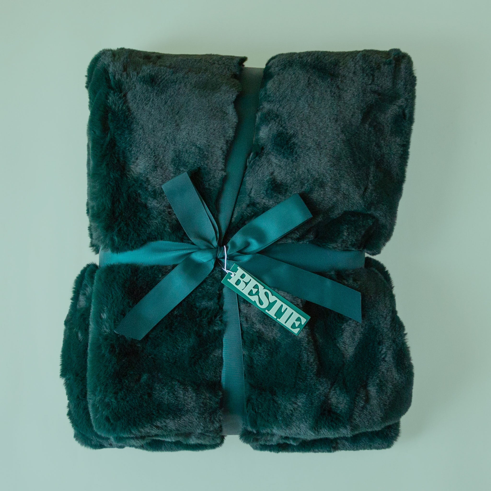 An emerald fur blanket with a satin ribbon and a mint tag that reads "bestie" tied onto it.
