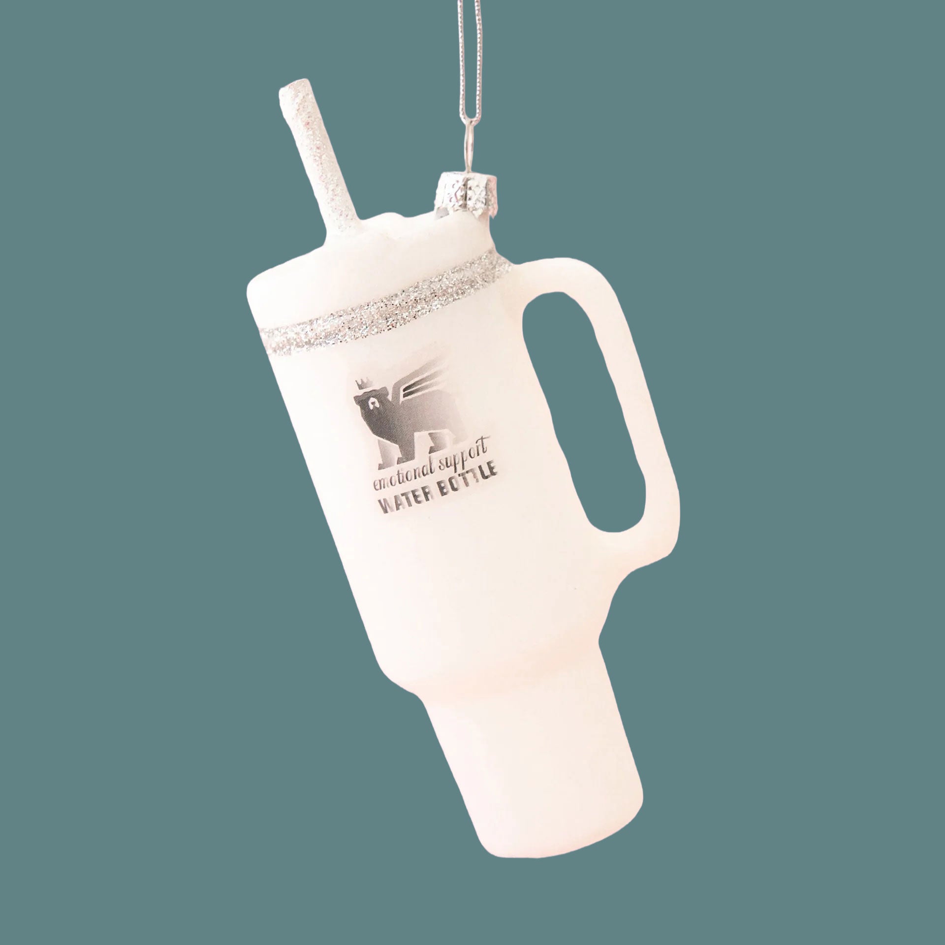 A white drinking tumbler ornament shown against a blue background. The lid and straw have silver sparkle details. 