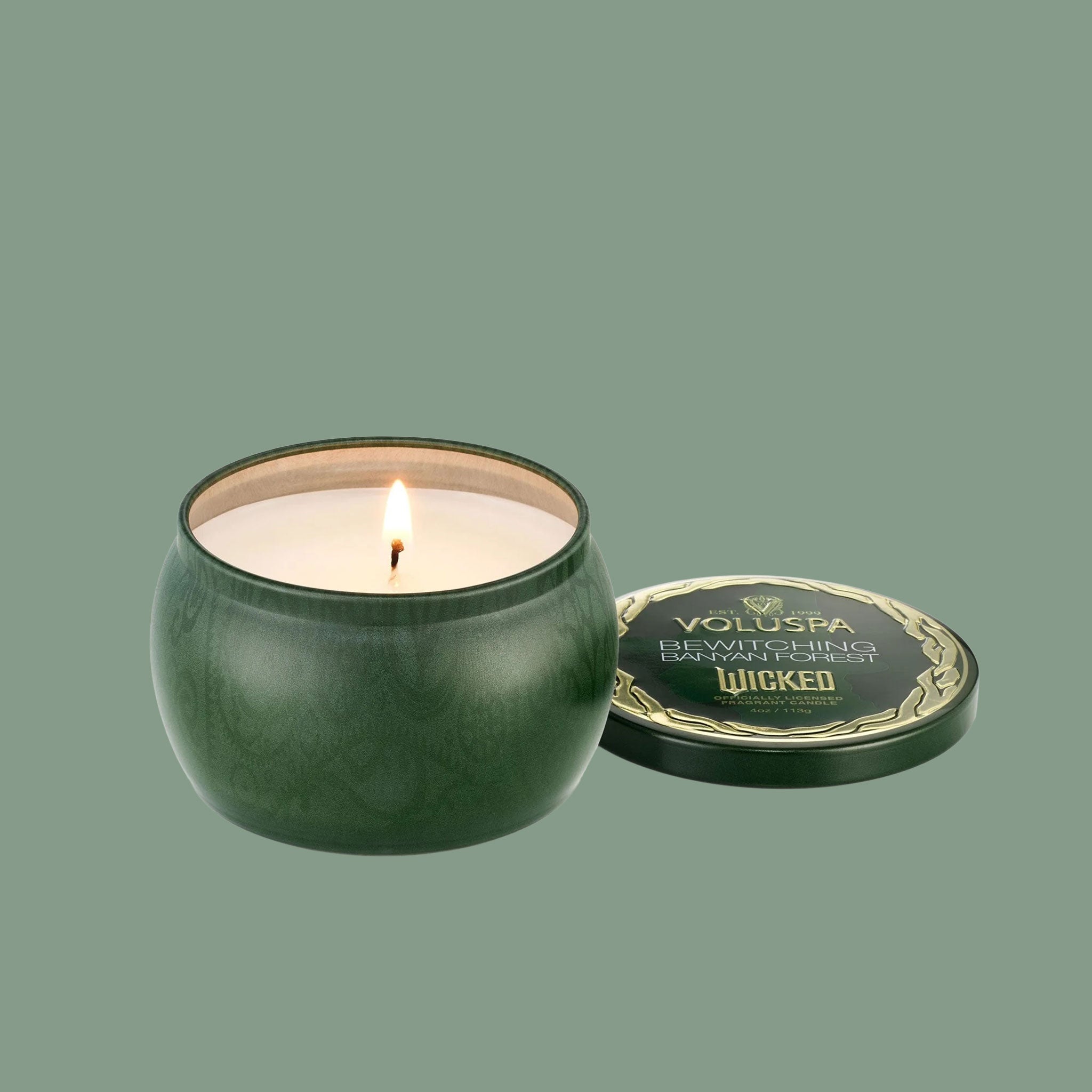 A green tin candle with gold details that reads, 'Voluspa, Bewitching Banyan Forest' Wicked. 