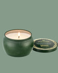 A green tin candle with gold details that reads, 'Voluspa, Bewitching Banyan Forest' Wicked. 