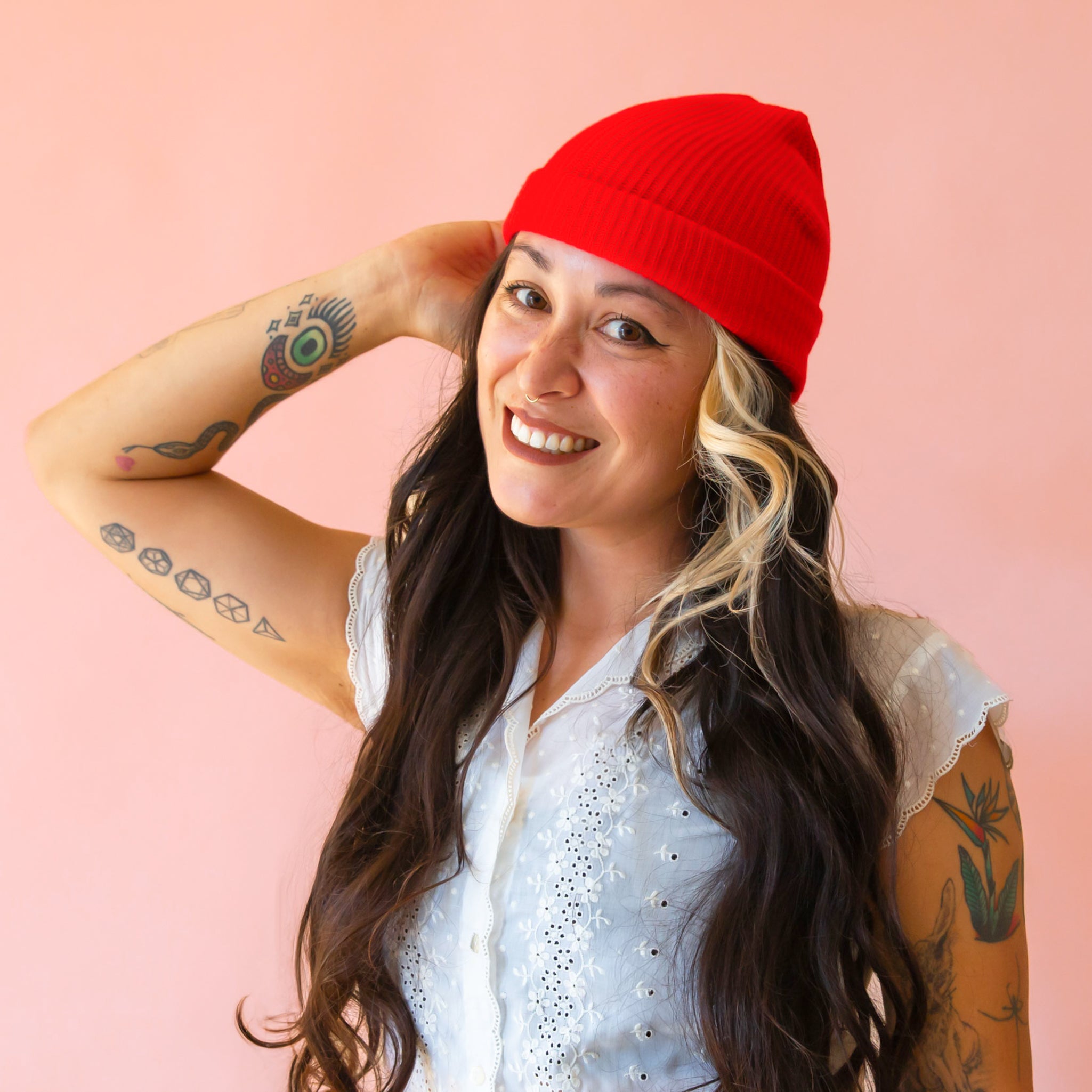 A brunette woman wears a bright red ribbed beanie. 