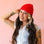 A brunette woman wears a bright red ribbed beanie. 