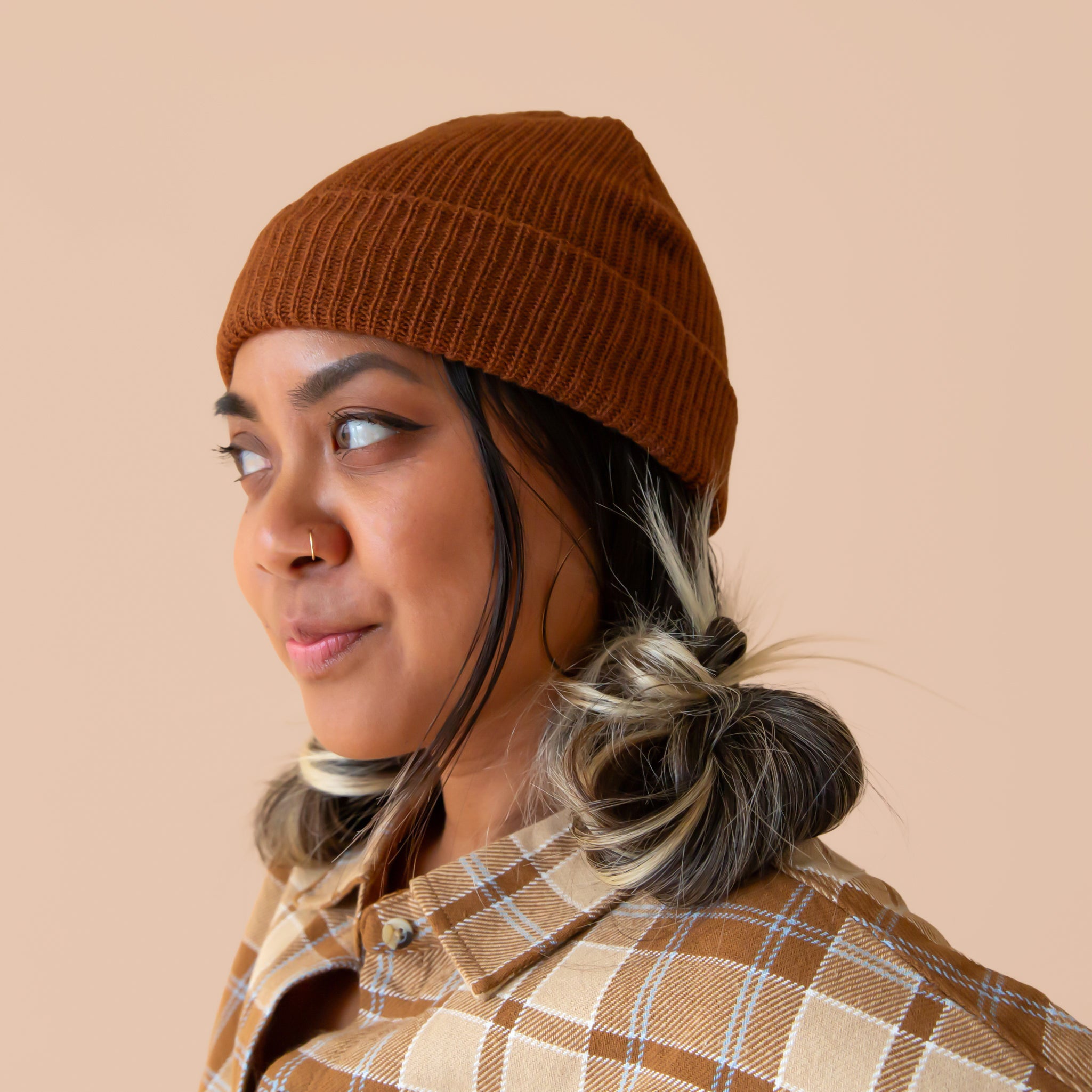 A woman wears a chocolate brown colored beanie and a flannel shirt.