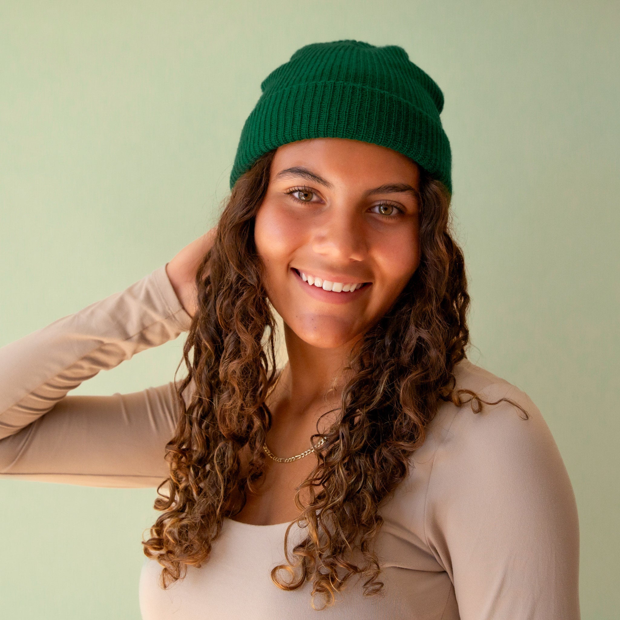 An emerald colored knit beanie sits on a green background.