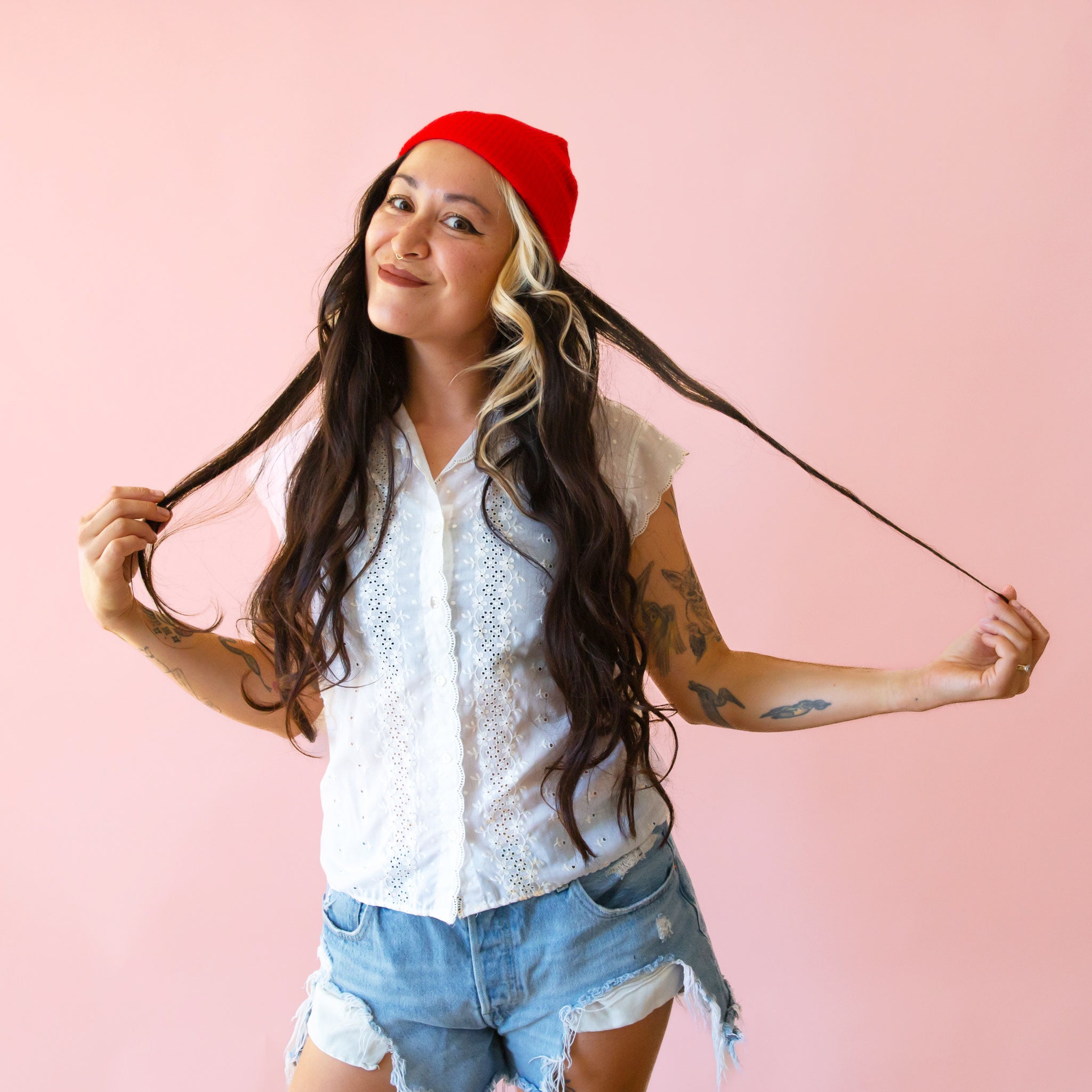 A woman in denim shorts wears a bright red ribbed beanie. 