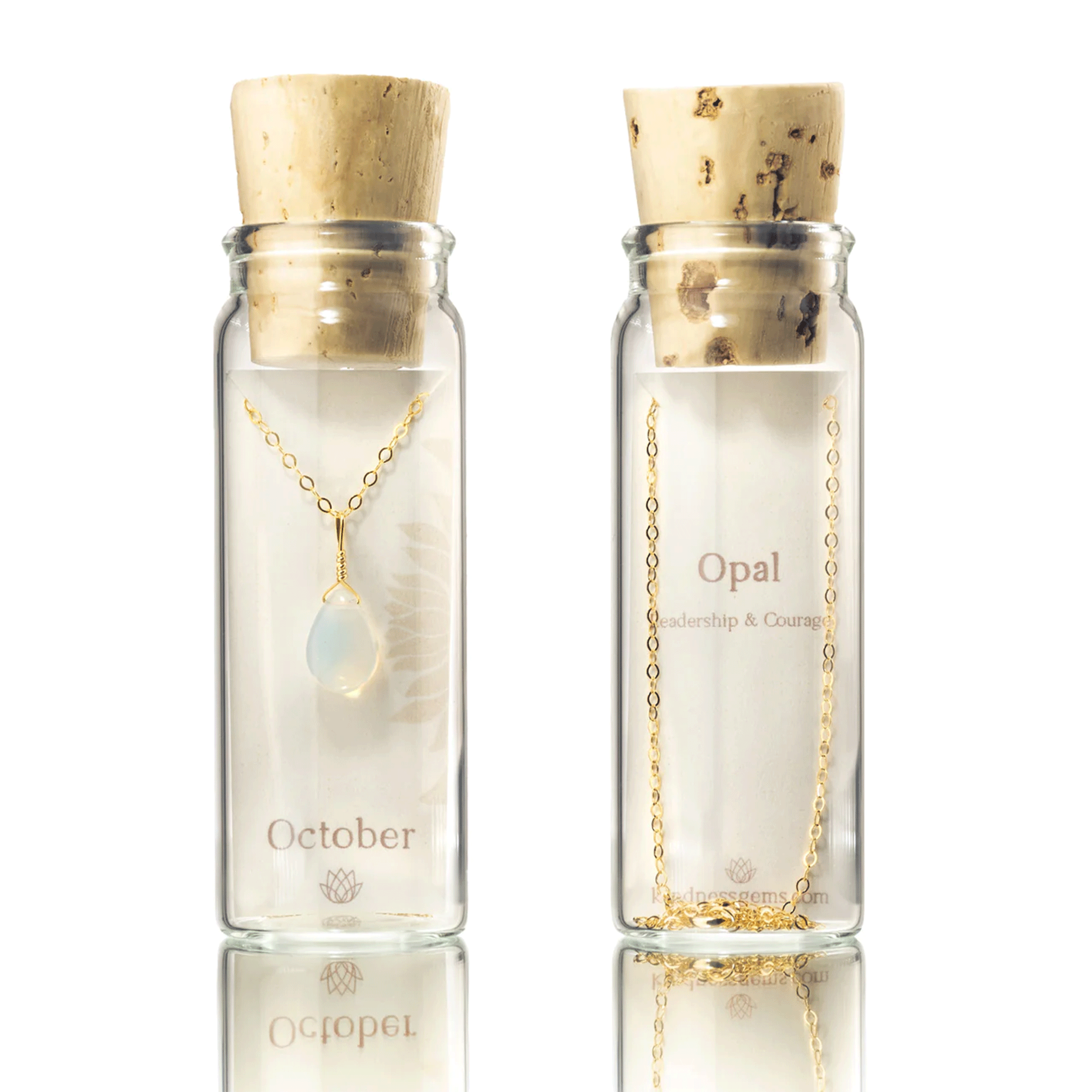 On a white background is a clear glass bottle with a cork top filled with a gold chain necklace with an opal October birthstone teardrop shaped gem in the center. 