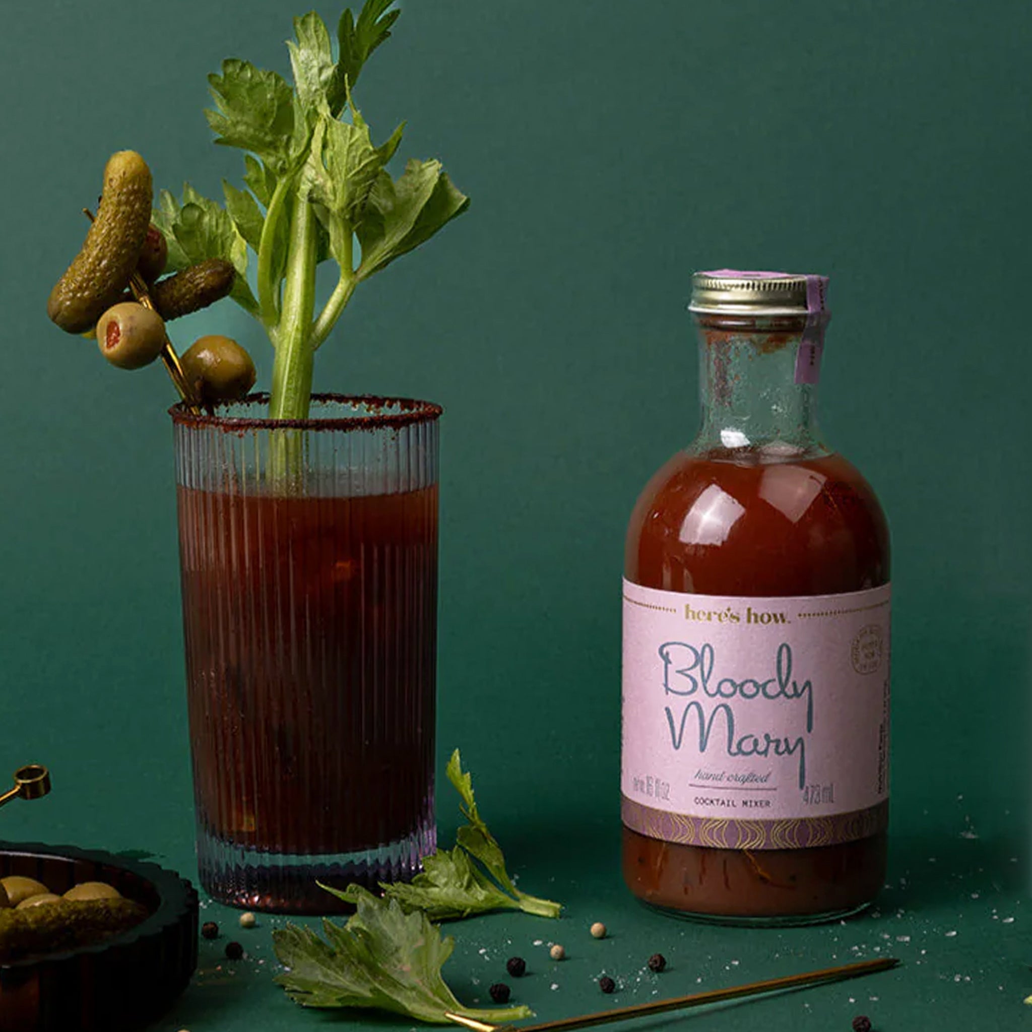 A glass bottle of bloody mary mix with a pink label and a gold lid. 