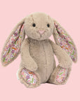 A beige bunny shaped stuffed animal toy with a floral pattern in the ears and on the feet.