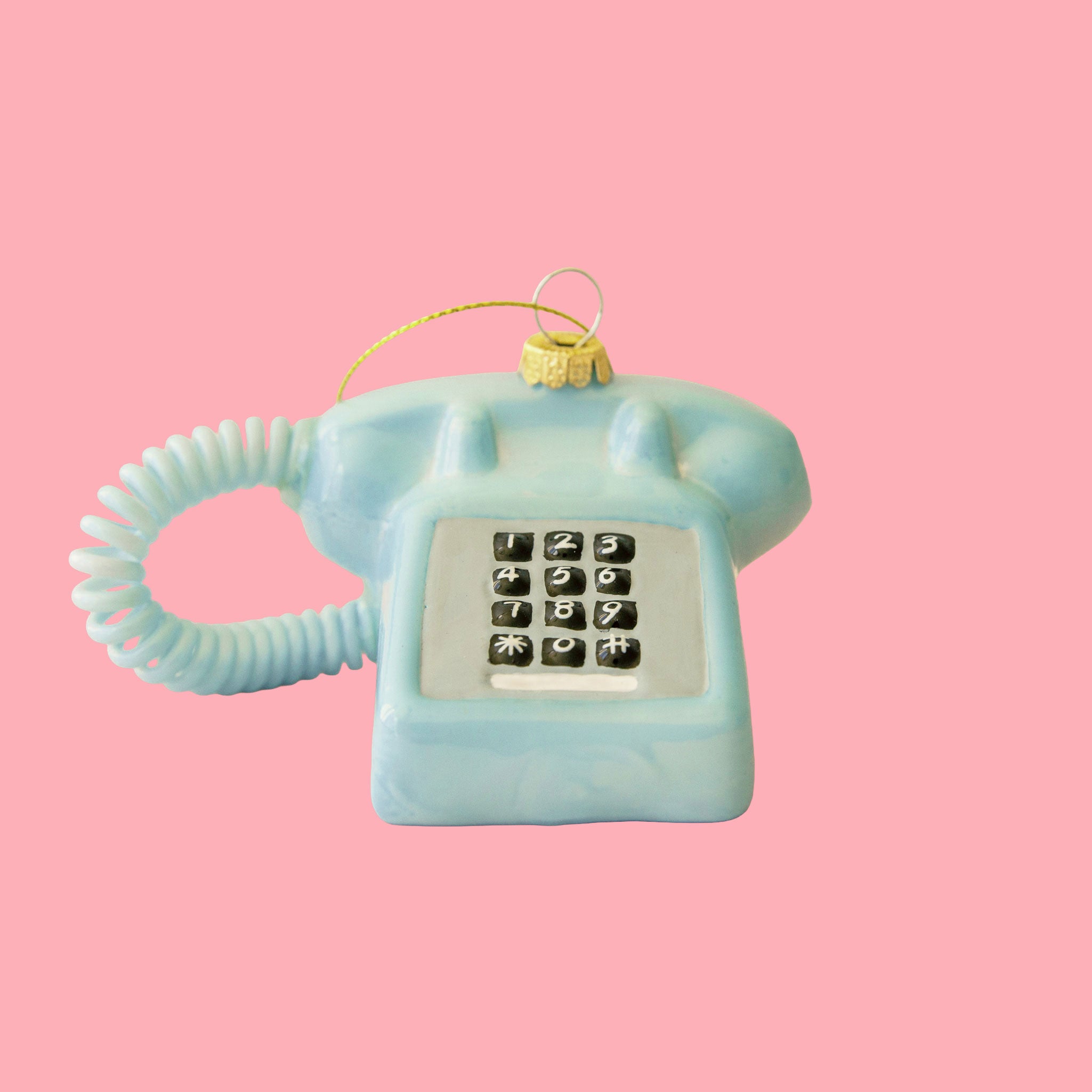 A blue rotary phone ornament on a pink background.