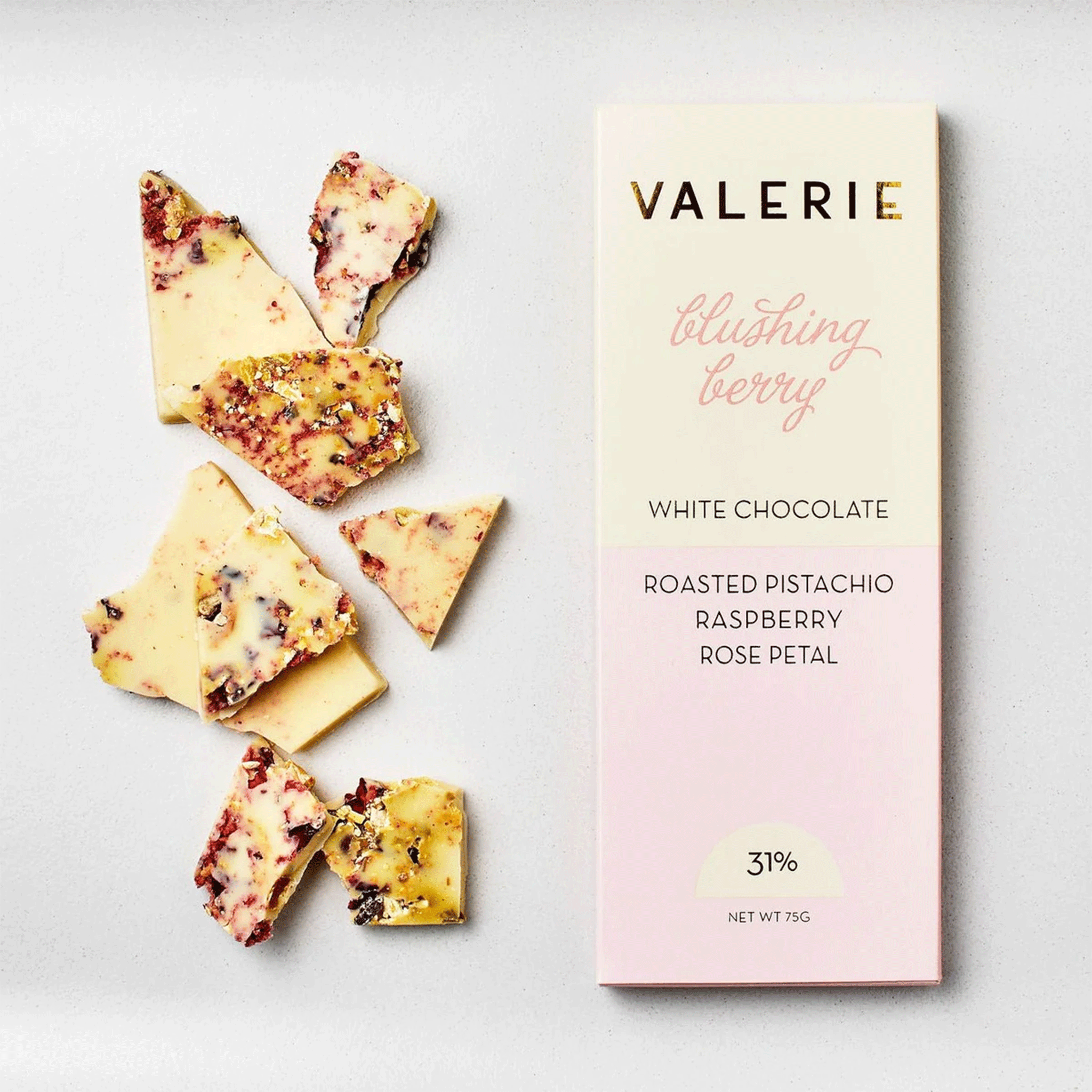 On a white background is a light pink and ivory packaged white chocolate bar that reads, &quot;Valerie blushing berry White Chocolate Roasted Pistachio, Raspberry, Rose Petal&quot;. 