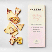 On a white background is a light pink and ivory packaged white chocolate bar that reads, "Valerie blushing berry White Chocolate Roasted Pistachio, Raspberry, Rose Petal". 