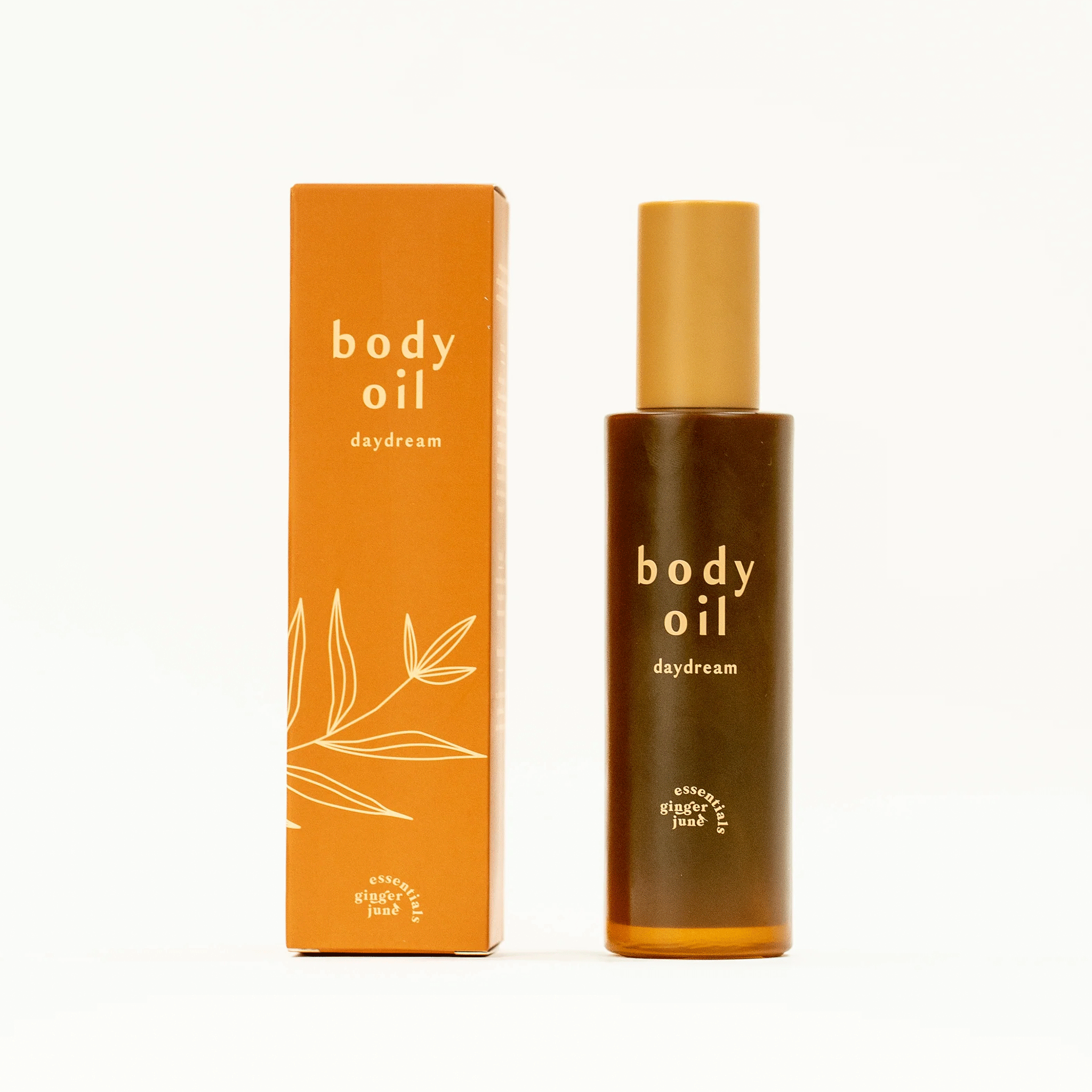On a white background is a bottle of body oil with a tan cap and an orange box packaging along with text on the front that reads, "body oil daydream". 