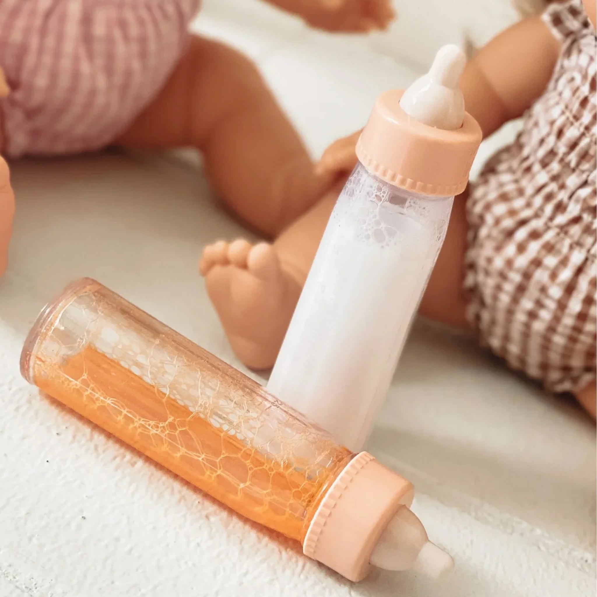 Two toy bottles, one with white liquid and the other with orange juice. 