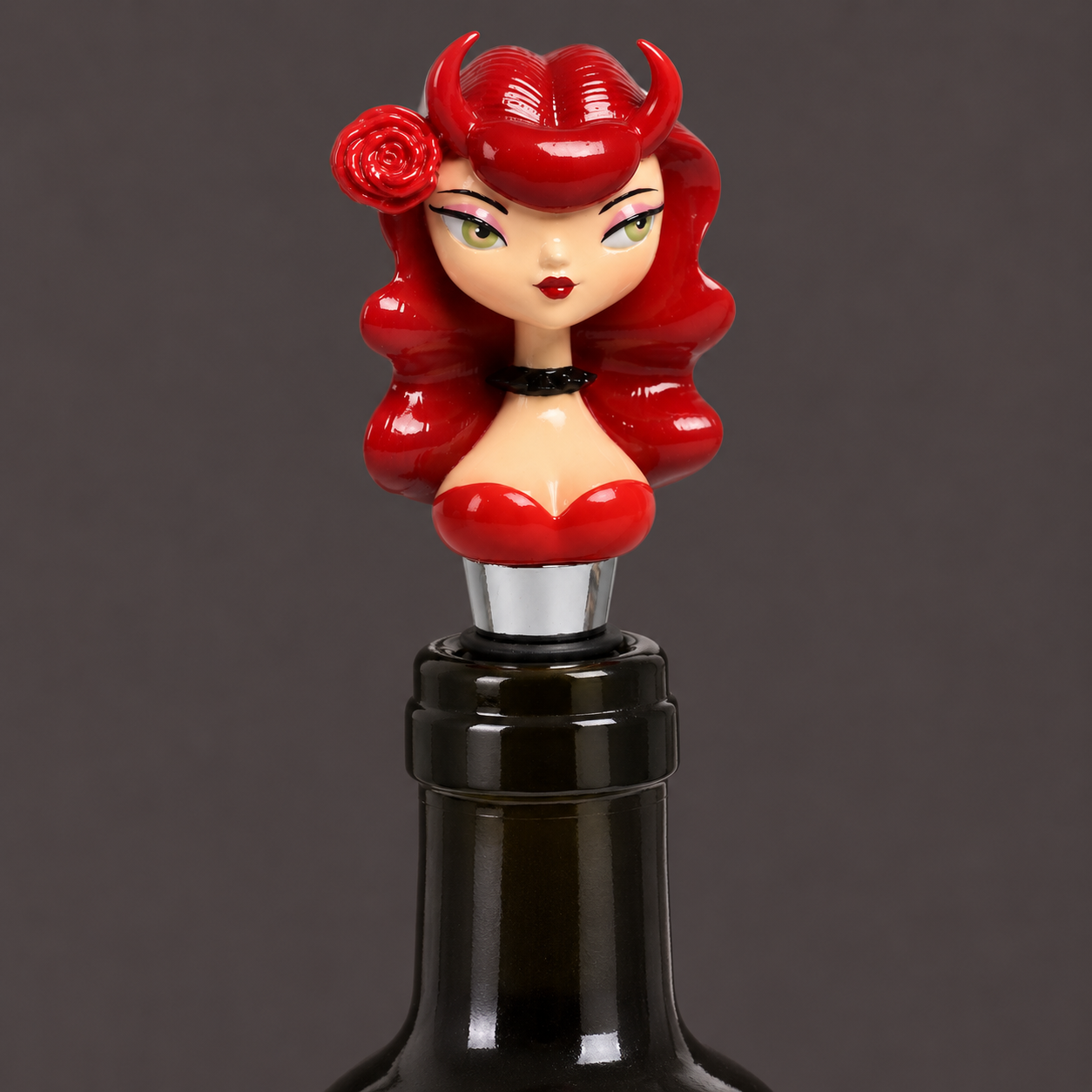 A novelty wine bottle stopper featuring a stylized pin-up doll head with bright red hair, horns, and a red top, mounted on a black rubber seal and silver metal spike against a dark gray background.