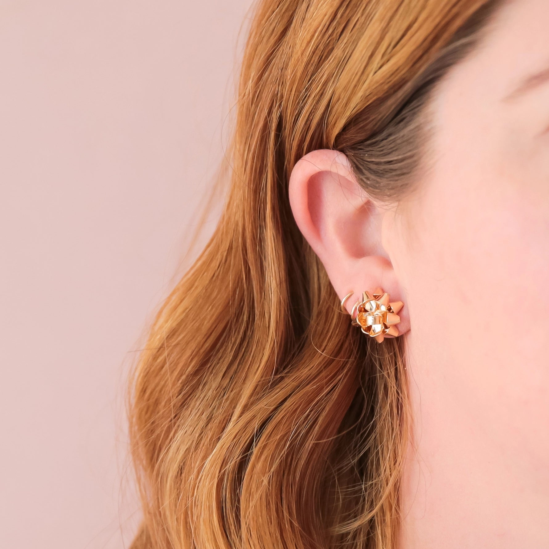 On a peachy background is a model wearing the gold bow earrings.