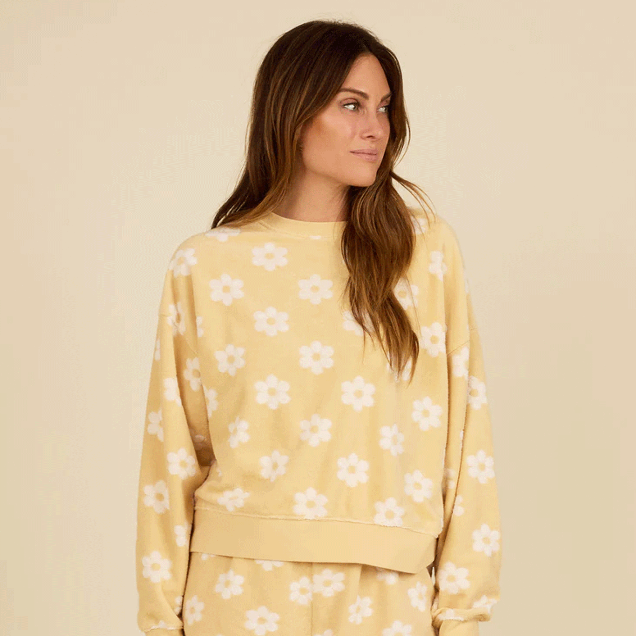 On a tan background is a yellow and ivory pullover sweatshirt with a daisy print all over. 