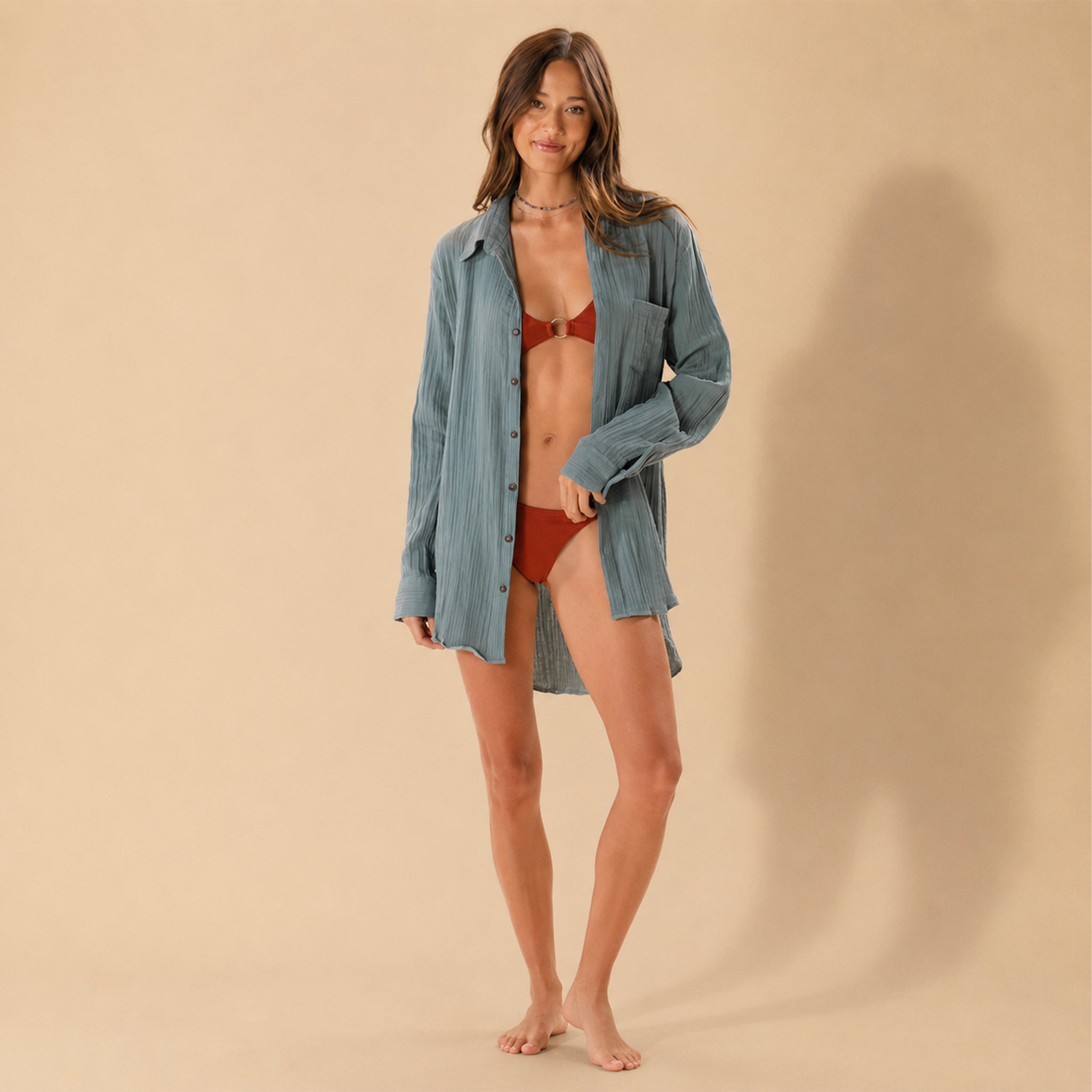 Woman wearing a blue shirt over a red bikini on a beige background