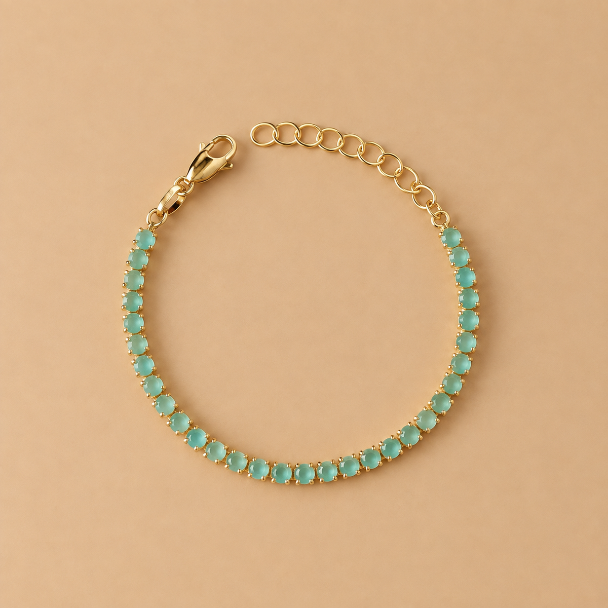 A gold tennis bracelet featuring small, round-cut light blue-green stones, displayed on a solid beige background.