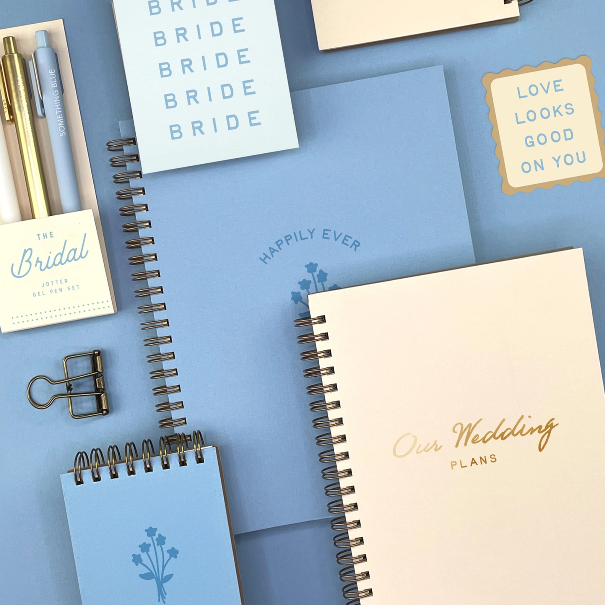 Wedding-themed stationery items including notebooks, cards, and a pen on a blue background.