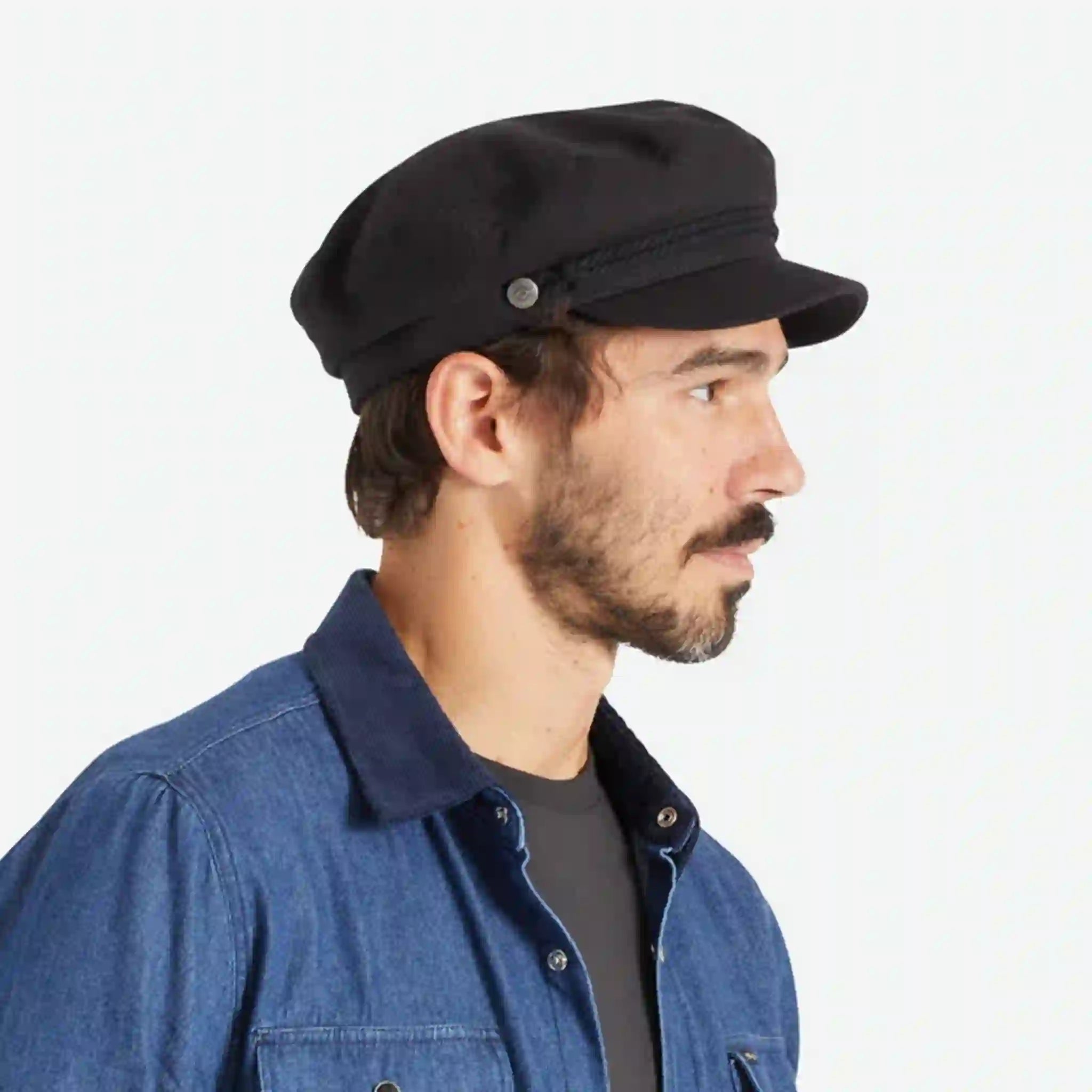 On a white background is a model wearing a black fiddler cap with a cord detail.