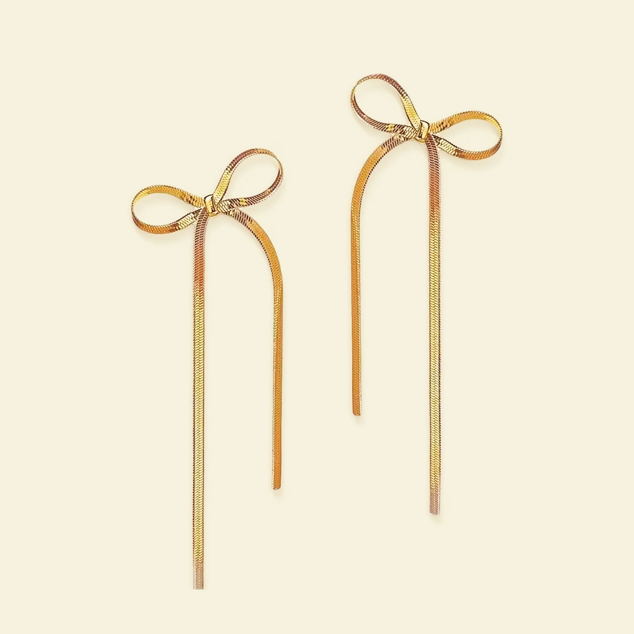 A pair of gold bow shaped earrings with dangles. 